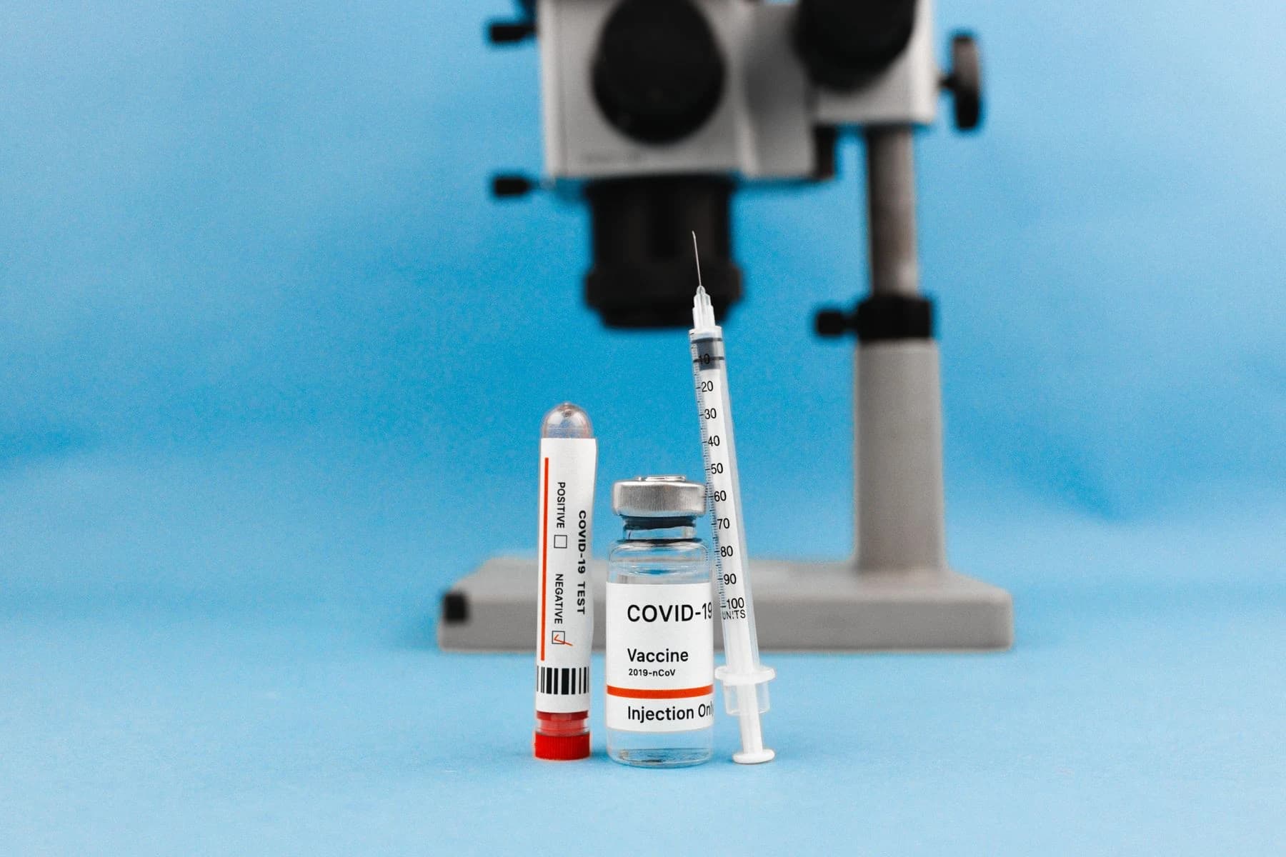 Mavi zeminde mikroskop önünde aşı flakonu, enjektör ve test tüpü